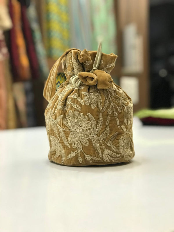 #Gold Decorative fabric pouch with floral patterns on a plain surface