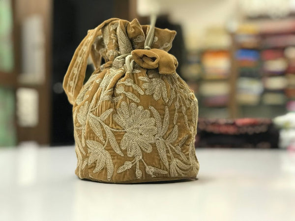 #Gold drawstring bag with floral embroidery on a blurred background