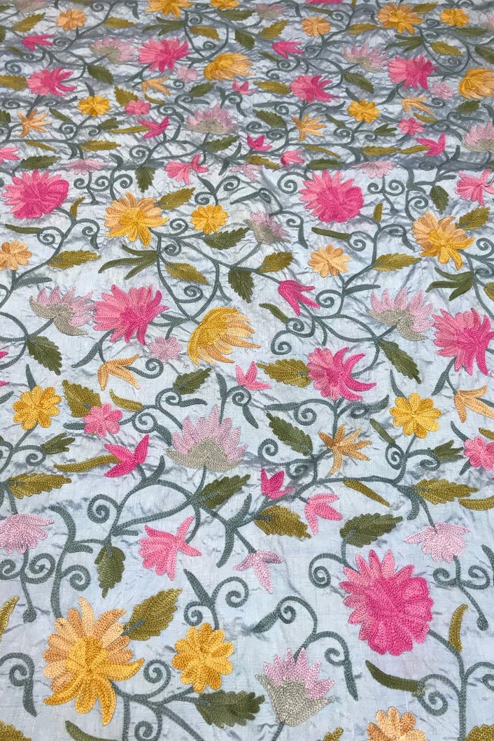 Embroidered fabric with floral patterns in pink, yellow, and green on a blue background
