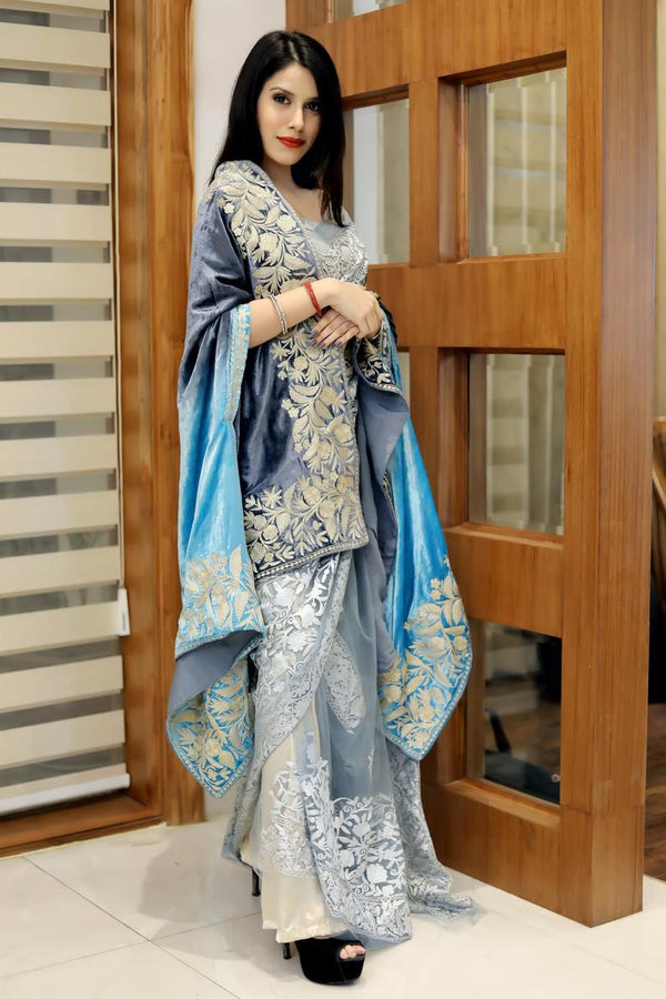 Woman in traditional embroidered outfit standing in a room with wooden door and striped wall.