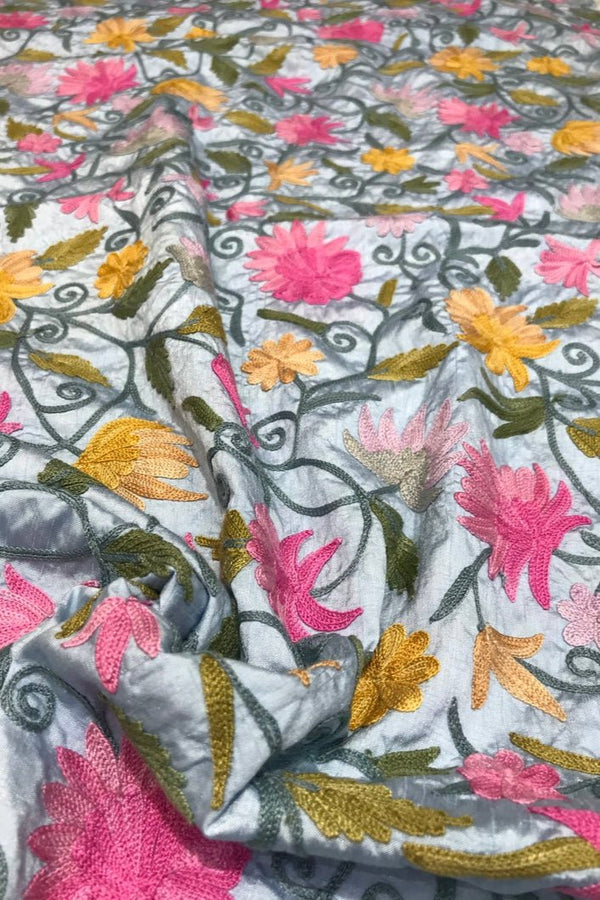 Embroidered fabric with floral patterns in pink, yellow, and green on a blue background